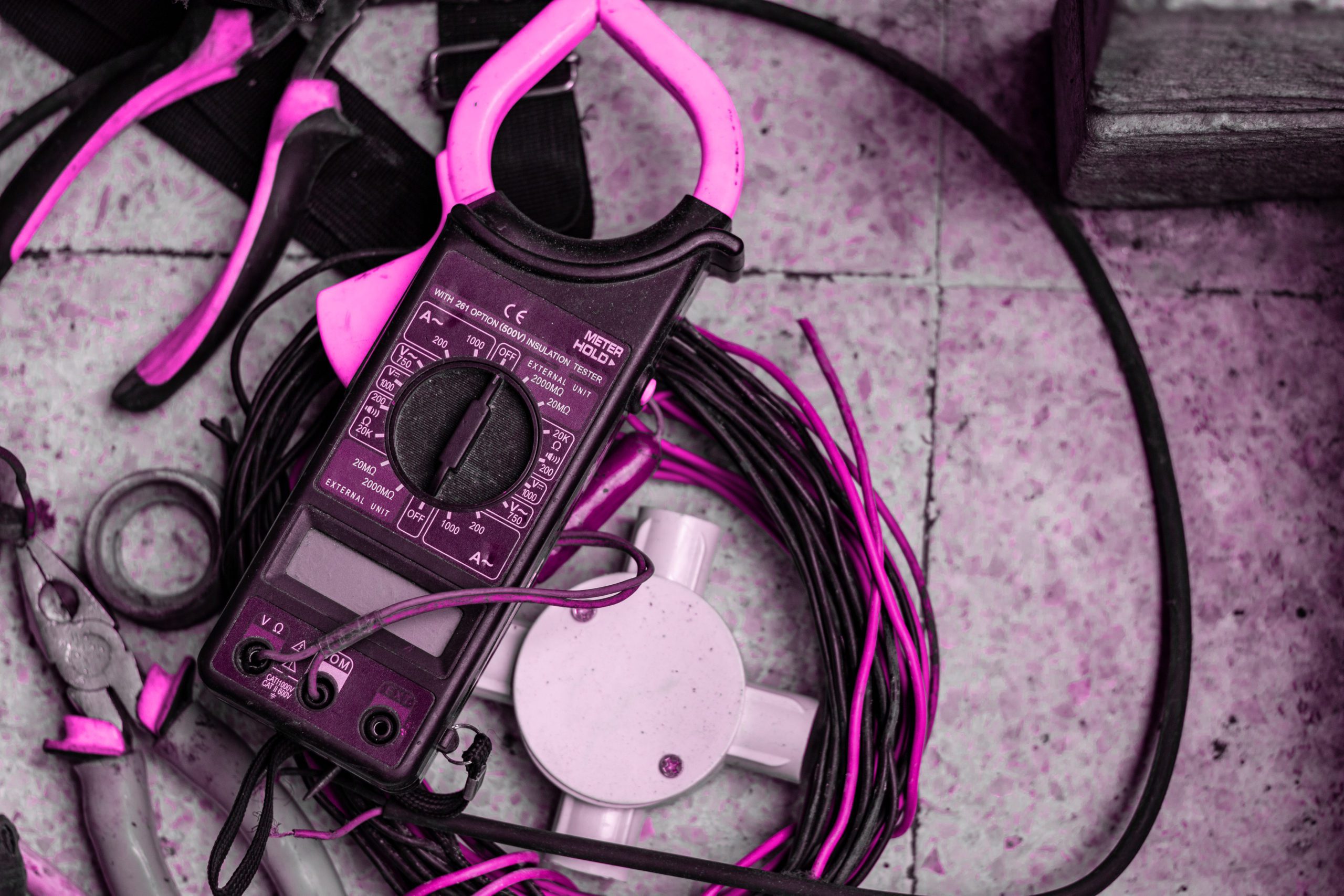Pink filtered image of an electrical meter and a pile of wires on a stone floor - service and panel upgrades Moncton