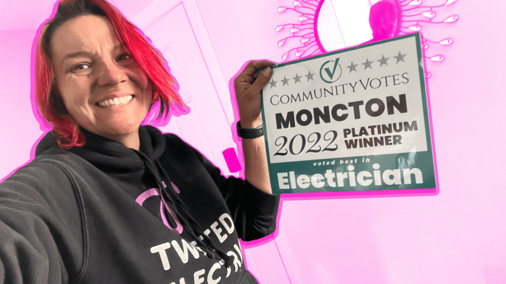 Tina Young (electrician) wearing a Twisted Electric hoodie and holding up her 2022 Platinum winner award from Community Votes Moncton as best Electrician on a pink tinted background